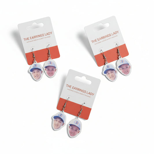 Three pairs of earrings with face-shaped charms on a gray surface.