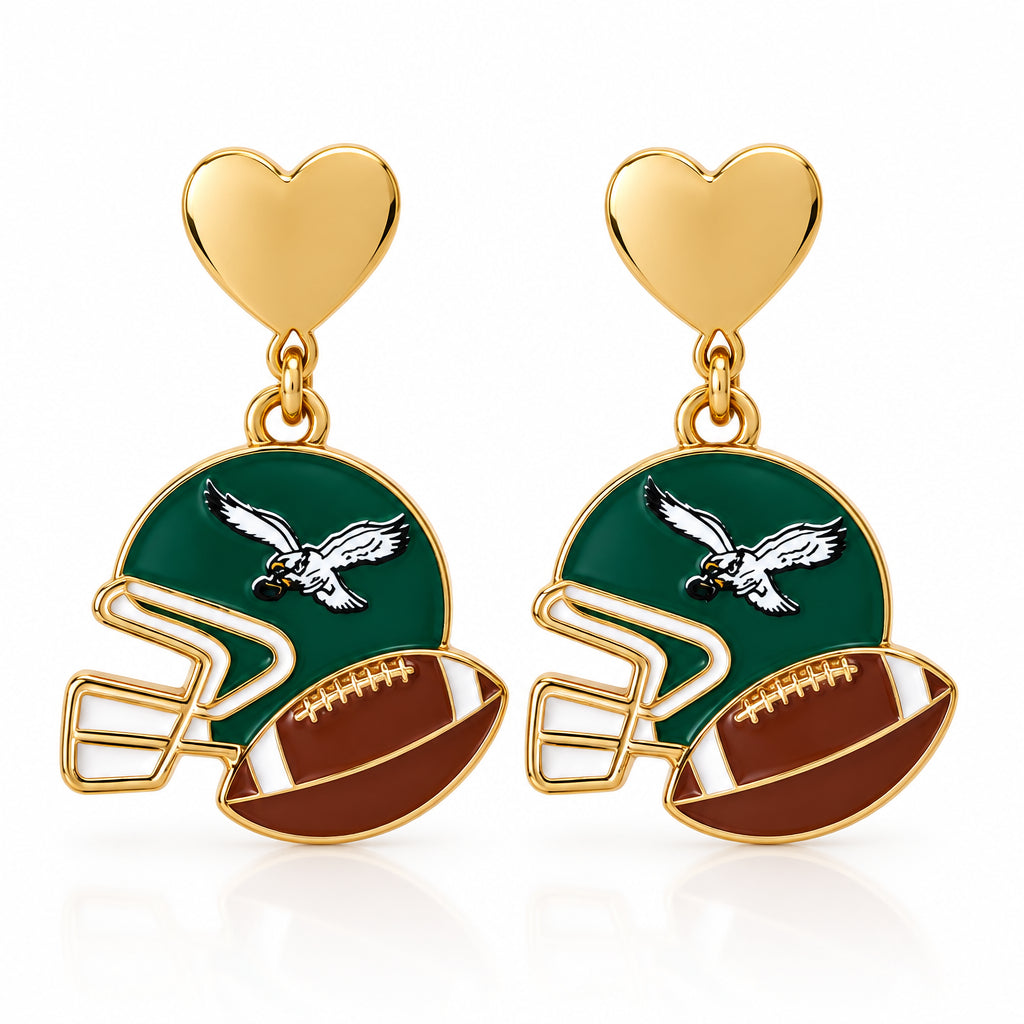 A pair of football helmet drop earrings with gold heart studs, displayed on a white and orange card labeled 'THE EARRINGS LADY'. The helmets are green and brown with white and gold details.