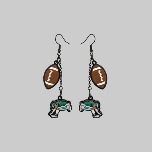 Hand holding a pair of earrings with football and elephant designs against a gray background