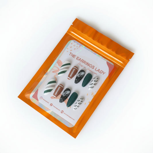 A set of 10 press-on nails displayed inside an orange holographic zip pouch on a black cutting mat. The nails feature various Philadelphia Eagles-themed designs including team logos and colors.