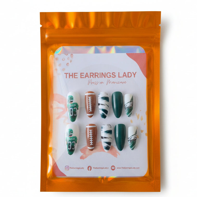 A set of 10 press-on manicure nails displayed on a white card inside an orange holographic pouch. The nails feature Philadelphia Eagles themed designs, including green jerseys with the number 33, footballs, and white nails with green stripes and team logos.