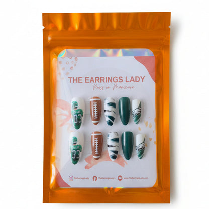 A set of 10 press-on manicure nails displayed on a white card inside an orange holographic pouch. The nails feature Philadelphia Eagles themed designs, including green jerseys with the number 33, footballs, and white nails with green stripes and team logos.