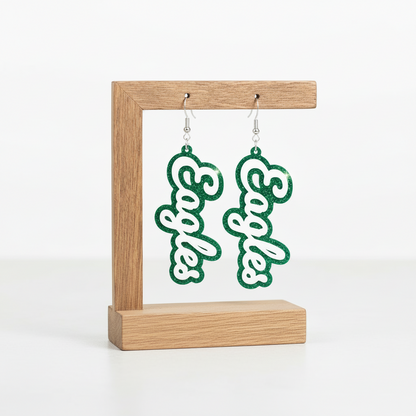 Pair of earrings with 'Eagles' text on a wooden stand with a natural background
