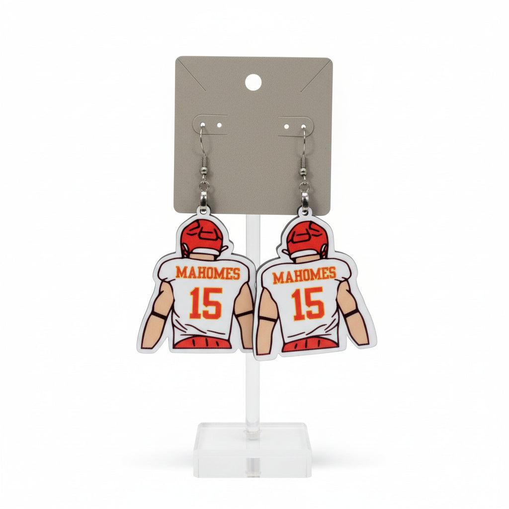 Earrings with sports jersey design on a card labeled 'The Earrings Lady' held by a hand in a mall. KC Earrings