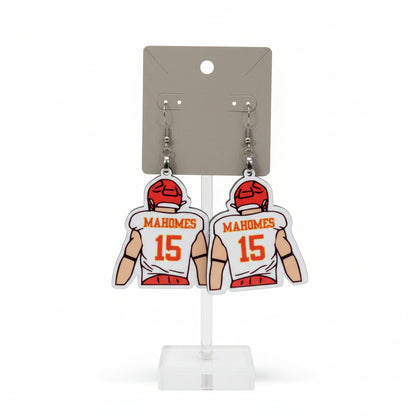 Earrings with sports jersey design on a card labeled 'The Earrings Lady' held by a hand in a mall. KC Earrings