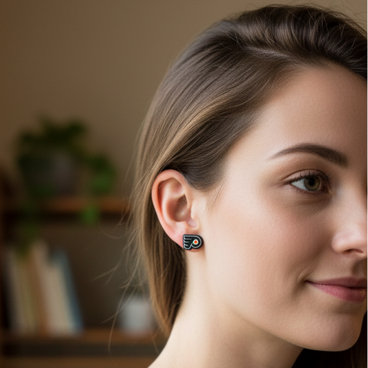 A woman in a gray knit top wearing a small black circular stud earring with a silver-toned inner ring, photographed in a softly lit indoor setting with a blurred bookshelf in the background.