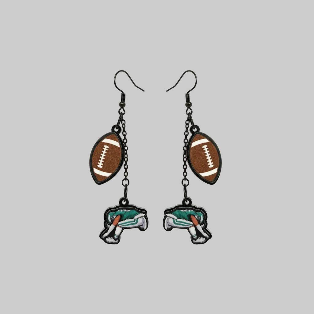 Hand holding a pair of earrings with football and elephant designs against a gray background