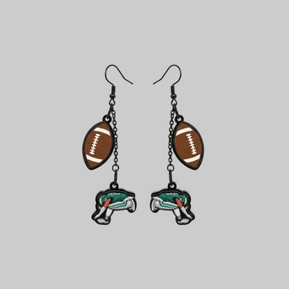 Hand holding a pair of earrings with football and elephant designs against a gray background