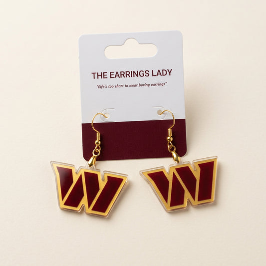 A pair of gold-tone drop earrings shaped like the Washington Huskies 'W' logo, featuring a dark red center with gold borders, displayed on a white and red backing card from 'The Earrings Lady'.