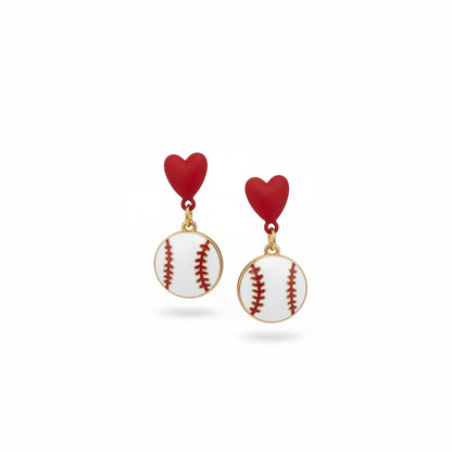 A hand holds a pair of handmade baseball-themed earrings on a white backing card from 'The Earrings Lady'. The earrings feature red heart studs and white baseball charms with red stitching.