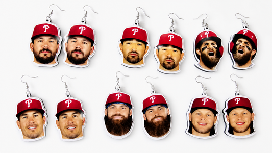 Twelve baseball-themed dangle earrings arranged in two rows on a light gray background. Each earring features a printed player face wearing a red Philadelphia Phillies cap, with silver-tone hooks above.