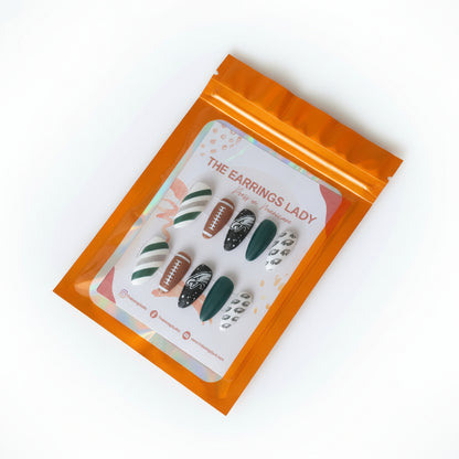 A set of 10 press-on nails displayed inside an orange holographic zip pouch on a black cutting mat. The nails feature various Philadelphia Eagles-themed designs including team logos and colors.
